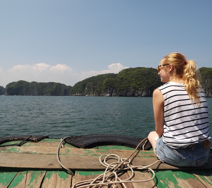 Halong Bay as seen from a green boat. Blog author sits looking out over the edge.